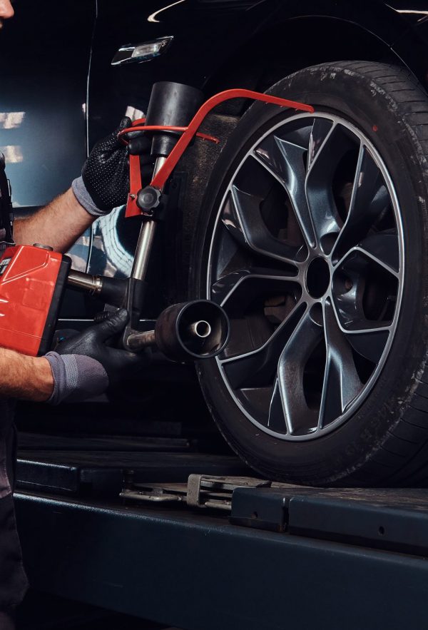 Man is doing balancing for tyres Muscular man is fixing car's wheel with special tool at auto service.